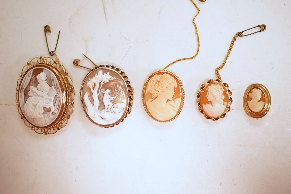 A collection of five cameo brooches, each of oval outline, set with a carved shell cameo, variously depicting three women in profile, a seated lady doing needlework, and a pastoral scene of a shepherd, longest 6.8cm, thr